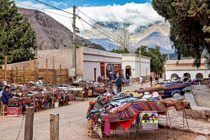 A marketplace with colorful fabrics and stalls in front of a majestic mountain landscape, tourist and souvenir market of Santa Rosa de Tastil near Salta in Argentina