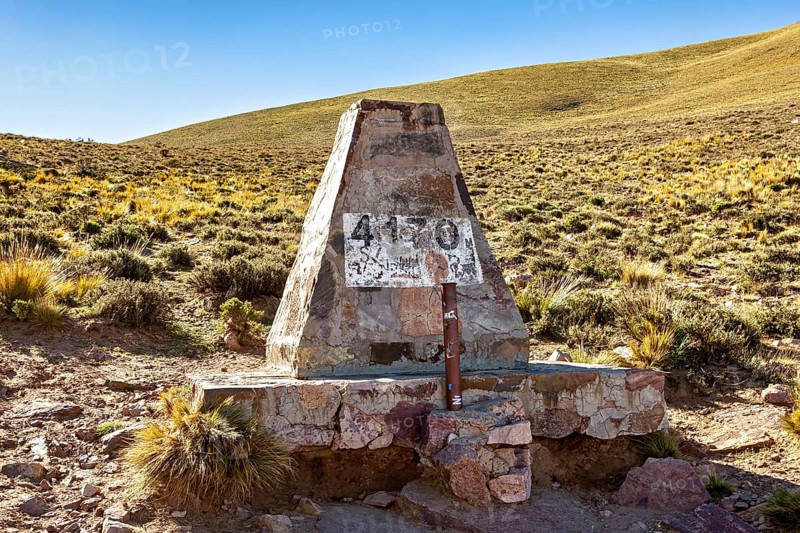 Stone pyramid with altitude marker at 4130 meters, surrounded by dry desert landscape under blue sky, monument on the Cuesta de Lipán pass in the province of Jujuy in northern Argentina