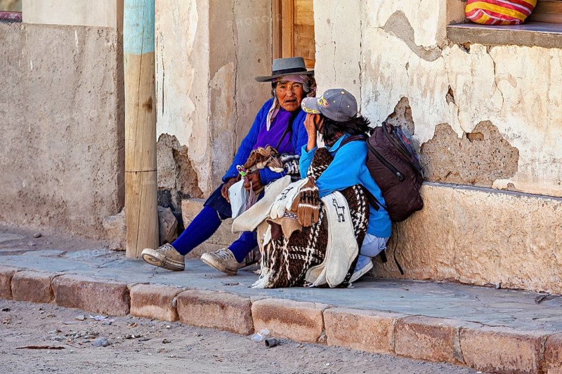Two woman in traditional clothes talking on a wall, people in the streets of San Antonio de los Cobres, Salta province, Argentina