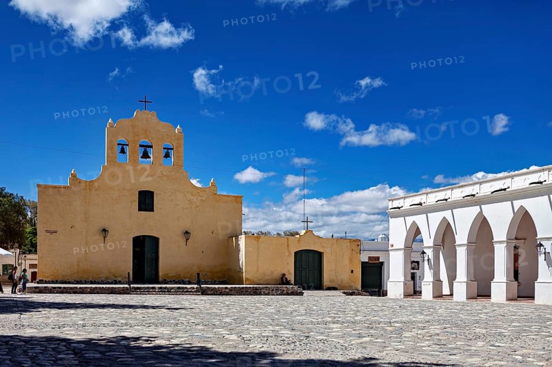 Yellow church with bell tower in front of a large square under bright blue sky, Iglesia San José de Cachi in Argentina