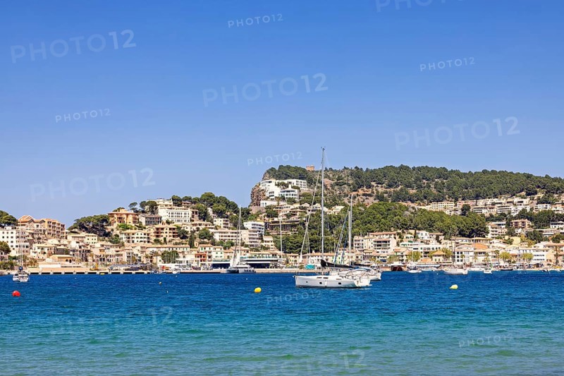 Scenic view of a coastal village with turquoise blue water and anchored sailboats and yachts and a hillside with residential and holiday buildings, Port de Soller, Mallorca, Spain