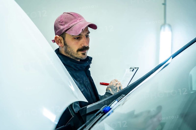 Auto repair shop worker checking a new vehicle, performing a meticulous inspection of the car body condition and noting down observations on a checklist