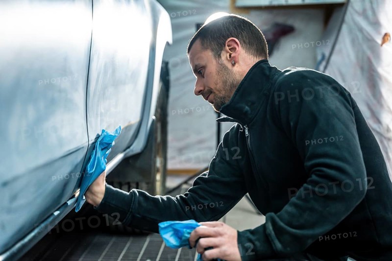 Focused mechanic carefully smooths and cleans car body surface before painting inside a modern auto repair and detailing workshop, ensuring precision and high quality vehicle finish