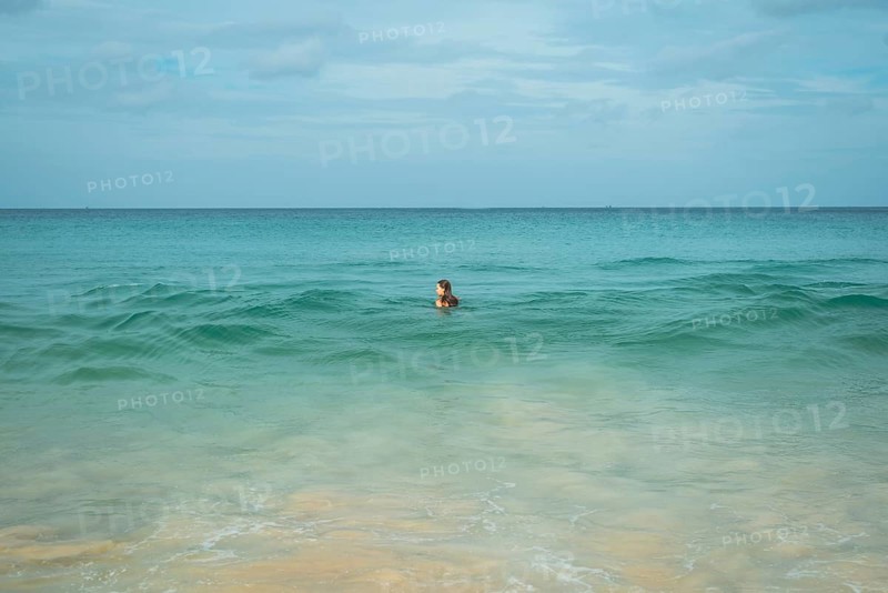 A young woman enjoys a swim in the clear turquoise waters of a tranquil beach in vacation, creating a peaceful scene with gentle waves, sandy shores, and a vast horizon in Thailand