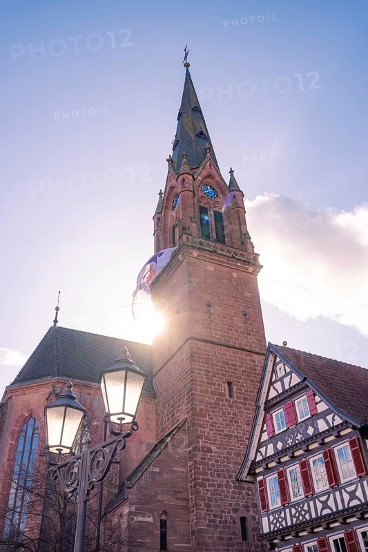 Church tower in sunlight next to a traditional half-timbered house under a clear sky, Calw, Calw district, Germany