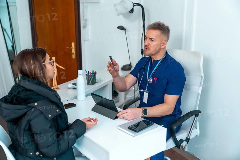 Doctor in scrubs having a conversation with a female patient during a medical consultation at a clinic office, providing information and discussing health issues