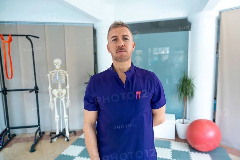 Physiotherapist standing confidently in a modern recovery clinic, offering sports osteopathy and medical rehabilitation amidst professional equipment and a skeletal model