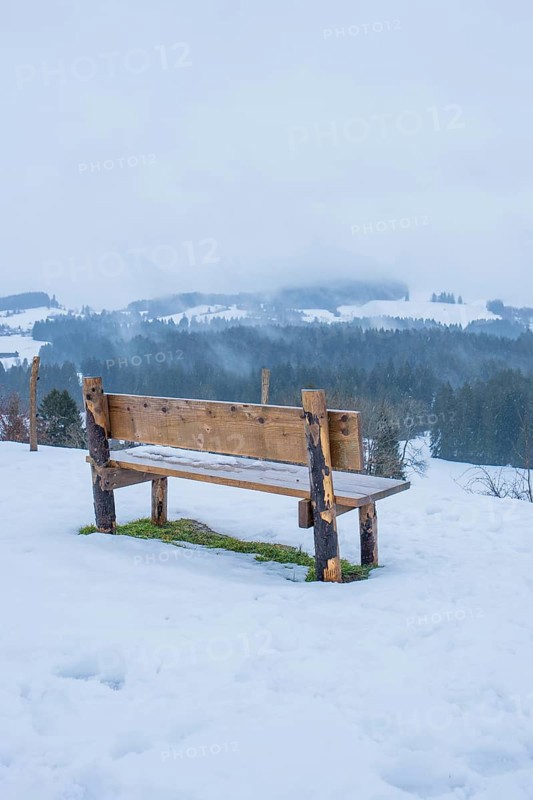 Wooden bench on snowy ground with a view of a quiet winter landscape, Sinnraum, Oberreute, Allgäu, Bavaria, Germany