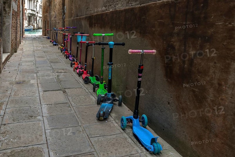Parked colorful children's scooters, scooters on a wall in front of a kindergarten, Venice, Veneto, Italy
