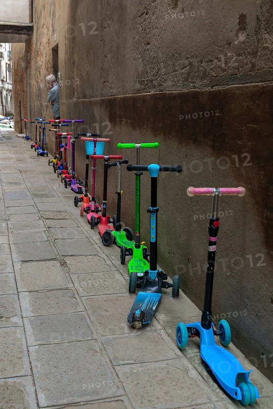 Parked colorful children's scooters, scooters on a wall in front of a kindergarten, Venice, Veneto, Italy