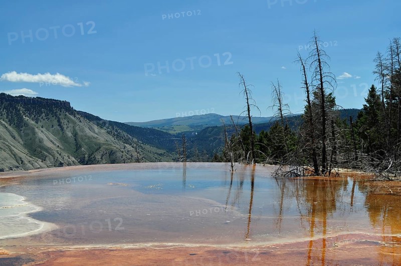 Natural pool with volcanic deposits and reflections and extensive views of mountains, Yellowstone National Park, Wyoming, USA