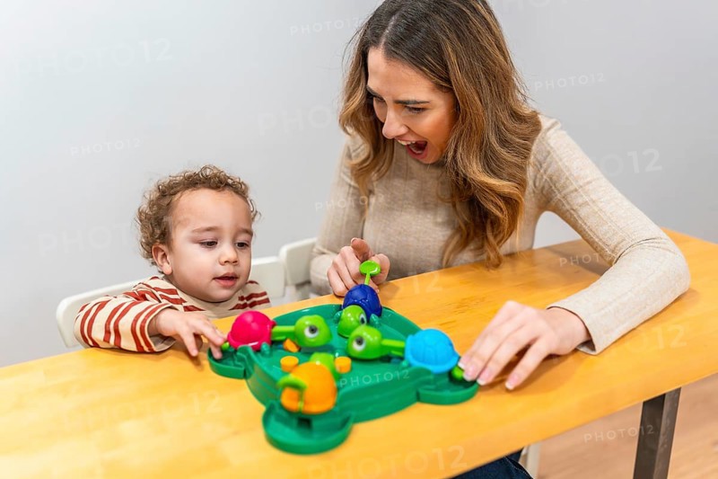 Happy mother and toddler play a colorful tabletop turtle game, smiling and learning together while bonding, exploring skills, concentration, and joyful discovery at home
