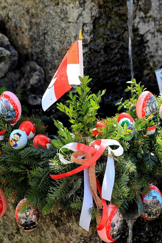 Detail of an Easter fountain in Franconian colors red and white, Franconian Switzerland, in Kleingesee, Gößweinstein market in the district of Forchheim, Upper Franconia, Bavaria, Germany, wreath with Easter eggs, spruce branches and Austrian flag as a festive decoration
