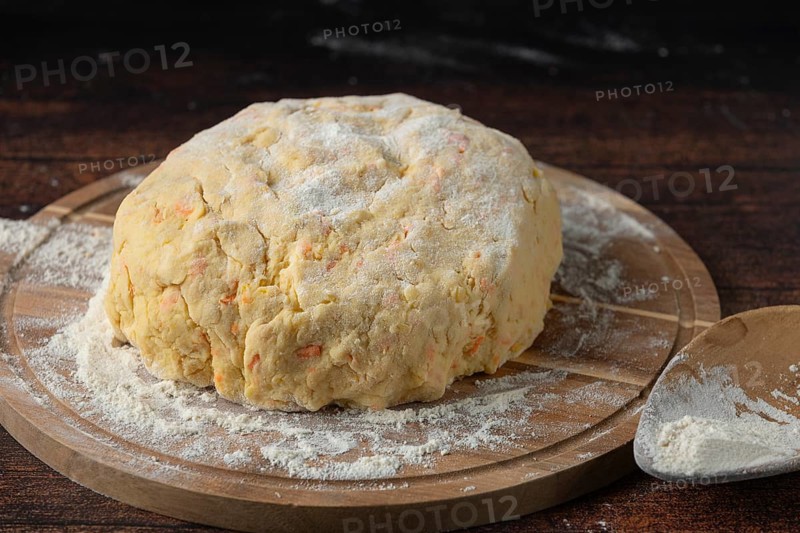 A lump of dough covered with flour on a wooden board in a dark kitchen