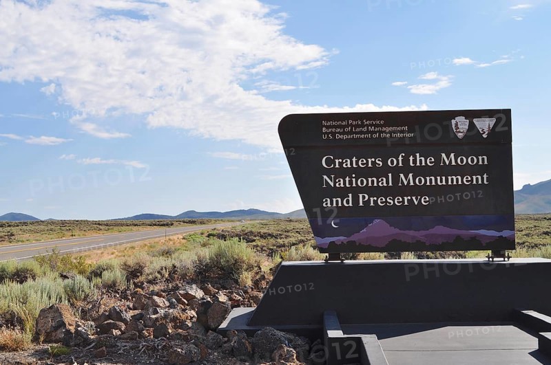 Craters of the Moon National Monument sign next to a road with wide landscape and blue sky, Craters of the Moon National Monument, Idaho, USA