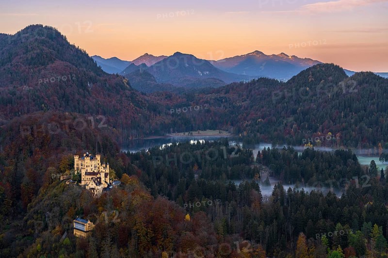 Scenic view of Hohenschwangau Castle amidst the vibrant autumn foliage of the Bavarian Alps The sunset casts a warm glow over the mountains and forested landscape