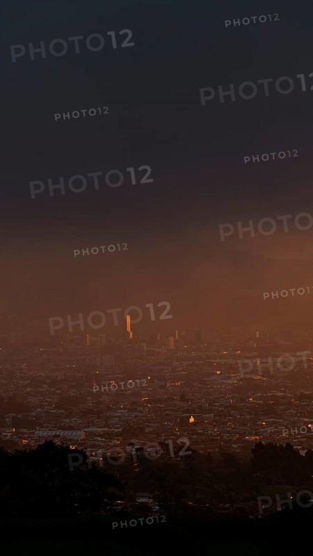 A serene sunset over San Jose, Costa Rica, captured from a mountain vantage point. The capital city bathes in a golden glow, evoking a peaceful urban evening
