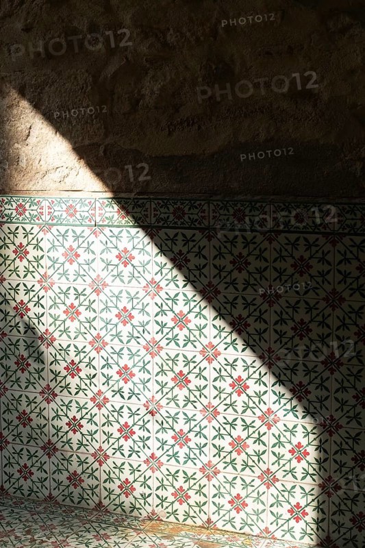 Sunlight splits across a wall covered in traditional Moroccan ceramic tiles, casting shadows and highlighting the intricate patterns