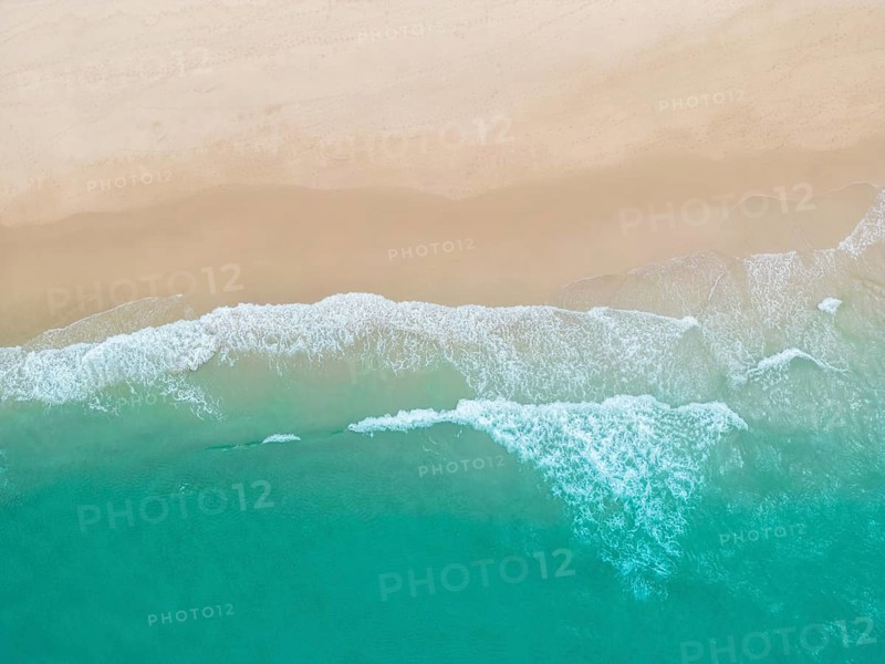 A breathtaking aerial photograph of a sandy beach in Portugal, where gentle turquoise waves meet the shore. Captures the natural beauty and tranquility of the Portuguese coastline