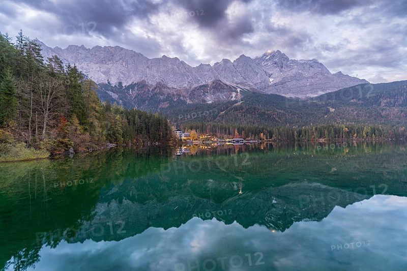 A breathtaking view of Eibsee at dusk, reflecting the towering Bavarian Alps and forested shoreline The tranquil waters and soft evening light create a serene alpine atmosphere