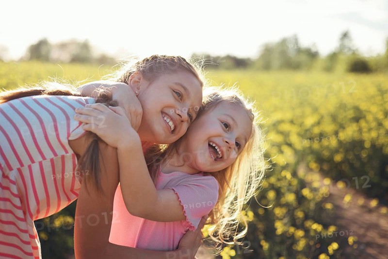 Two girls sisters play happily together in nature on a flowering field in summer