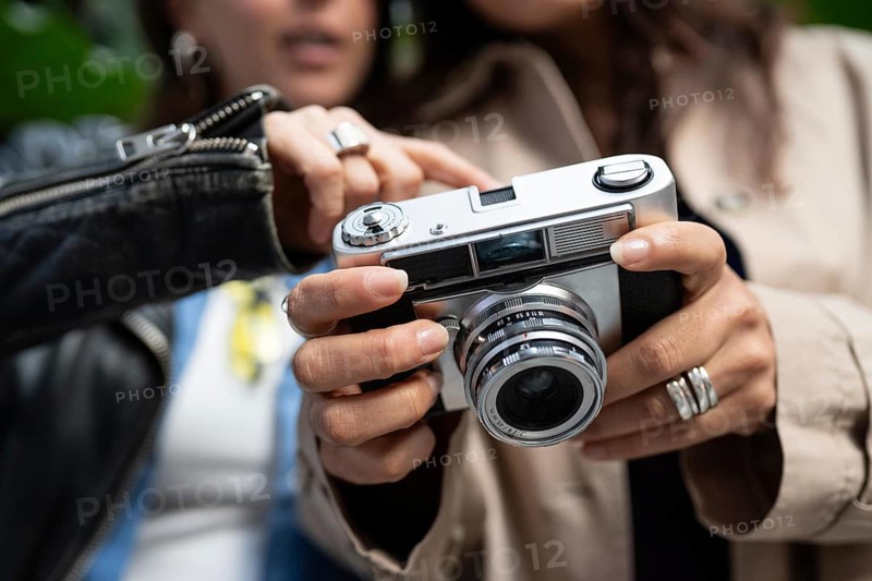 A lesbian couple shares a moment of connection through photography. Their hands hold a vintage camera, symbolizing creativity and love in an urban setting