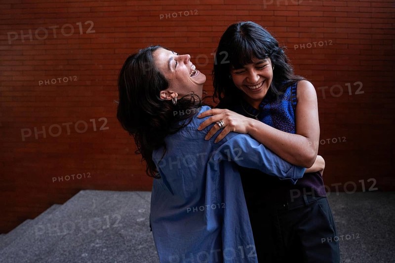 A joyful scene captures a multiethnic lesbian couple embracing and laughing together, celebrating their love and connection. Their happiness is palpable