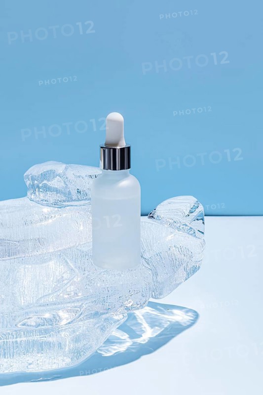 A frosted glass serum bottle with a dropper, resting in a carved ice block on a vibrant blue background, emphasizing cool freshness