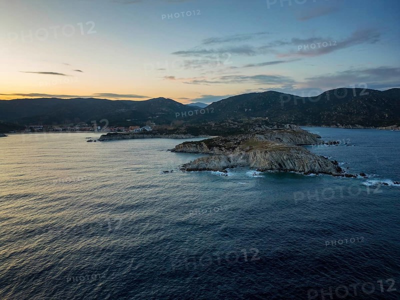 A scenic view of Kalamitsi village and beach in Greece at sunset. The rugged coastline, calm sea, and rolling hills create a peaceful and picturesque Mediterranean landscape