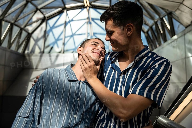 A loving gay couple shares a warm embrace on the streets of Madrid. Capturing genuine affection and connection, this image celebrates LGBTQIA+ pride in a lively urban setting