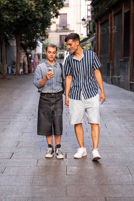 Stylish gay couple walking hand in hand on a quiet street in Madrid, Spain. One checks their smartphone while they enjoy a relaxed and casual stroll in the warm evening light