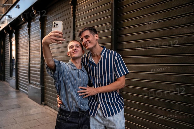 A joyful gay couple taking a selfie on the lively streets of Madrid. They express love and happiness, celebrating diversity in a vibrant urban setting