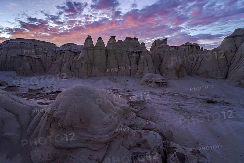 Stunning sunset illuminating the eroded sandstone formations in the Bisti/De-Na-Zin Wilderness, showcasing hues of purple and pink against the New Mexican landscape