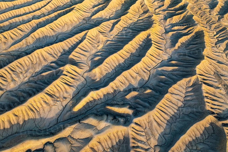 An aerial view of Caineville Mesa's golden desert textures in Utah at sunset. The rippled landscape forms a striking pattern, showcasing nature's artistic design