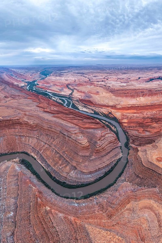Stunning aerial view of a winding river cutting through a vast desert in San Juan canyon. The rich red and orange hues of the San Juan canyon walls contrast with the blue sky above in Utah, USA