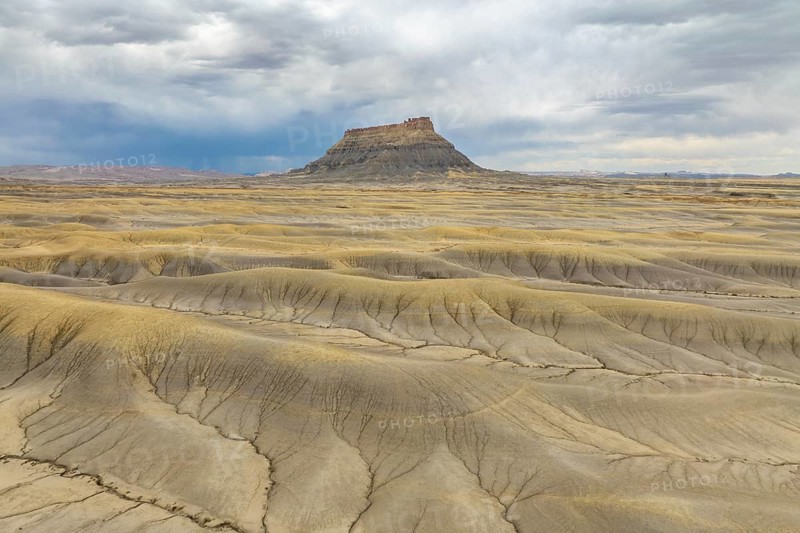 Vast desert landscape with a solitary rock formation under a dramatic sky in Hanskville, Utah. The terrain showcases natural patterns, displaying an array of textures and earthy colors of USA