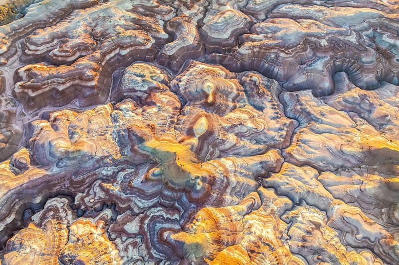 Aerial view of bentonite formations in Utah, USA, showcasing golden and earthy tones. The intricate patterns and textures create a unique, natural abstract art