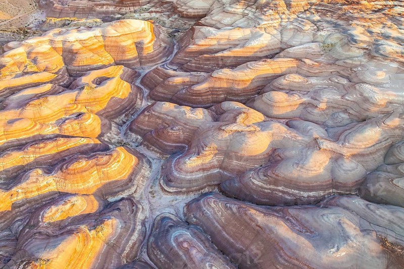 Aerial view of Utah's golden bentonite landscape, showcasing stunning layered earth tones and geological features. Light plays over rolling, stratified hills