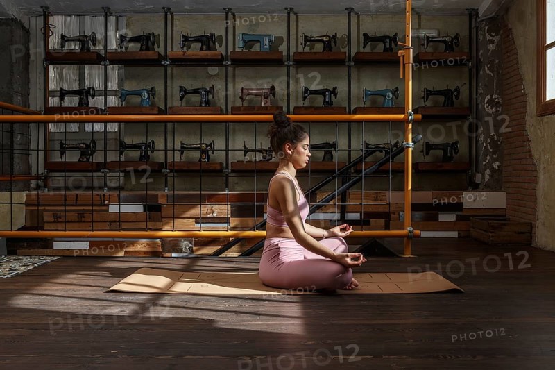 In a sunlit room filled with vintage sewing machines, a woman meditates on a yoga mat, practicing mindfulness and relaxation in serene harmony