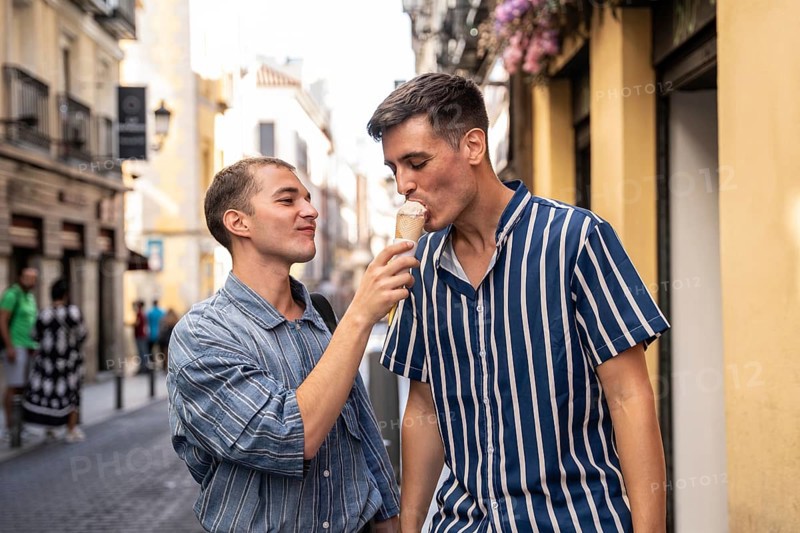 A joyful gay couple shares an ice cream on a lively street in Madrid, capturing the warmth and vibrancy of the city's culture and love for diversity