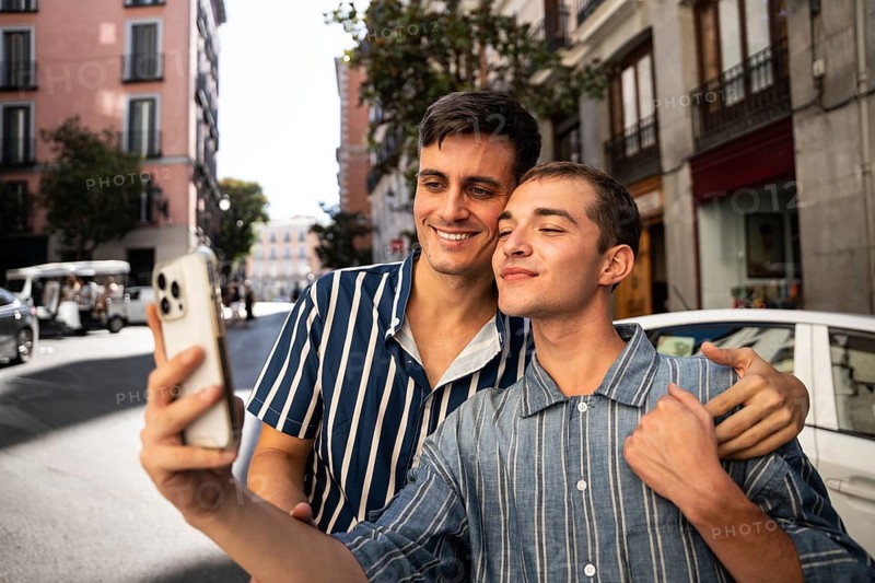 A gay couple happily takes a selfie while exploring the charming streets of Madrid. The vibrant cityscape enhances the joy and celebration of pride and LGBTQIA+ love