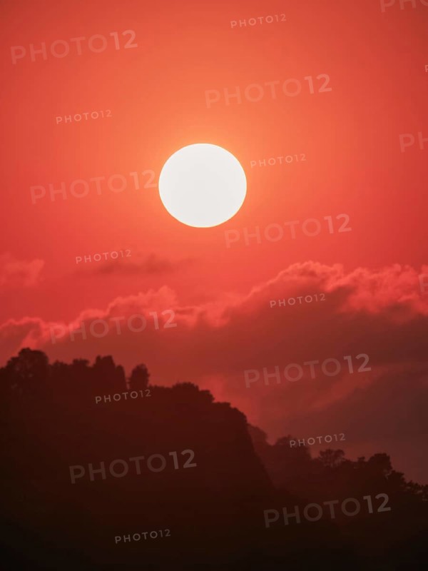 An ethereal orange sunset backlights a silhouette of mountainous terrain, expressive of untouched natural beauty and serenity
