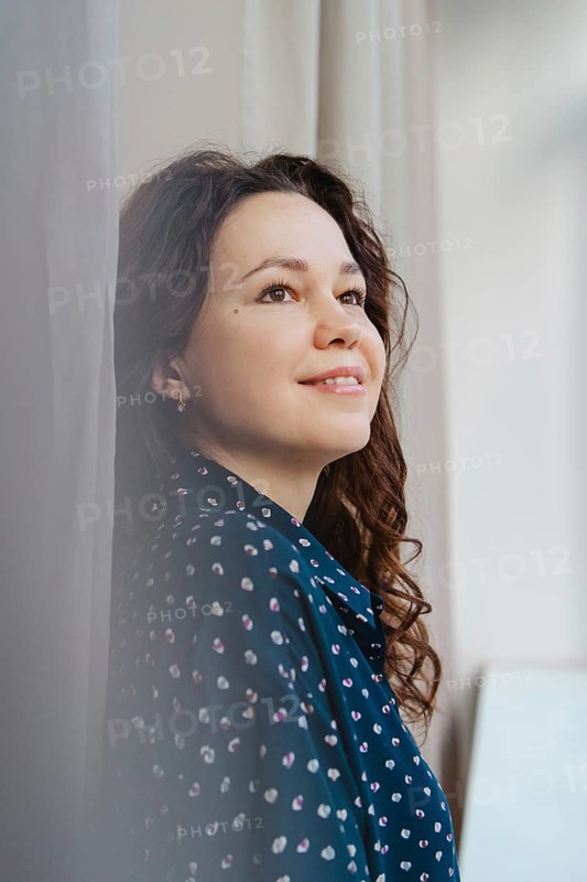 A woman in a patterned blue shirt gazes thoughtfully upward, bathed in soft natural light, creating a serene and introspective mood. Perfect for themes of contemplation and positivity
