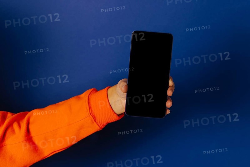 Crop hand of anonymous person holding smartphone with black screen against blue background