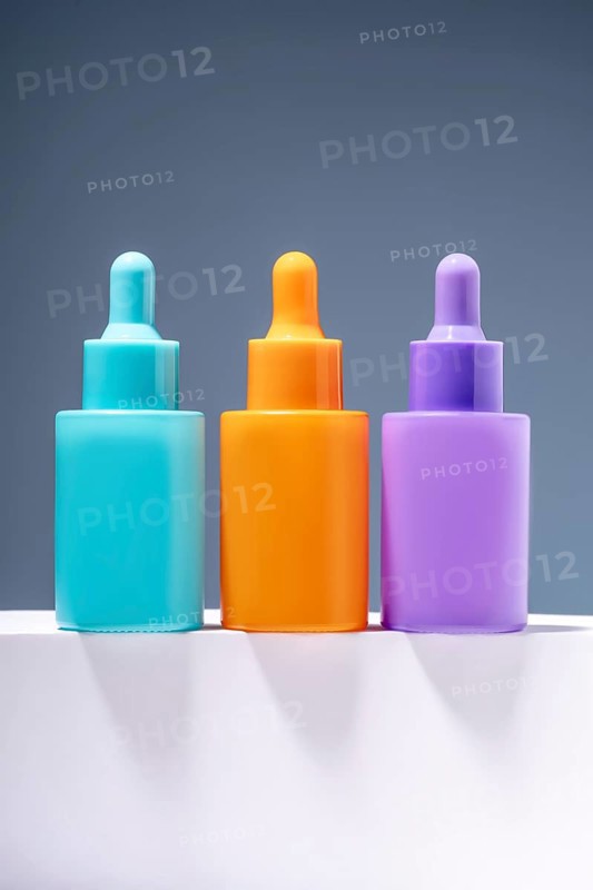 Three vibrant and colorful serum bottles aligned on a sleek surface with a soft gray gradient background, emphasizing modern aesthetics in skincare packaging