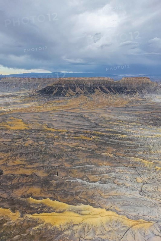 Aerial view of a rugged desert landscape featuring mesas under a cloudy sky in Hanskville, Utah. The diverse earth tones create a dramatic visual. Perfect for nature and geology themes of USA