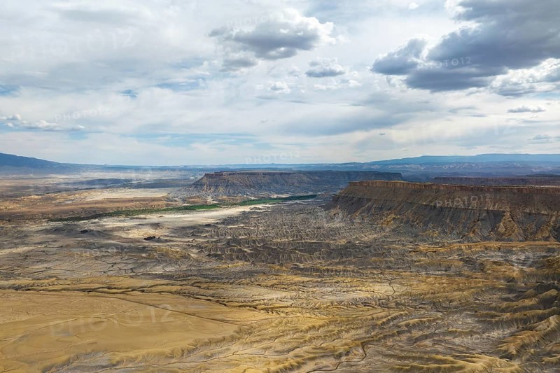 Aerial view of a rugged desert landscape under a dramatic, cloud filled sky in Hanskville, Utah. The image features eroded terrains, cliffs, and expansive vistas, highlighting nature raw beauty