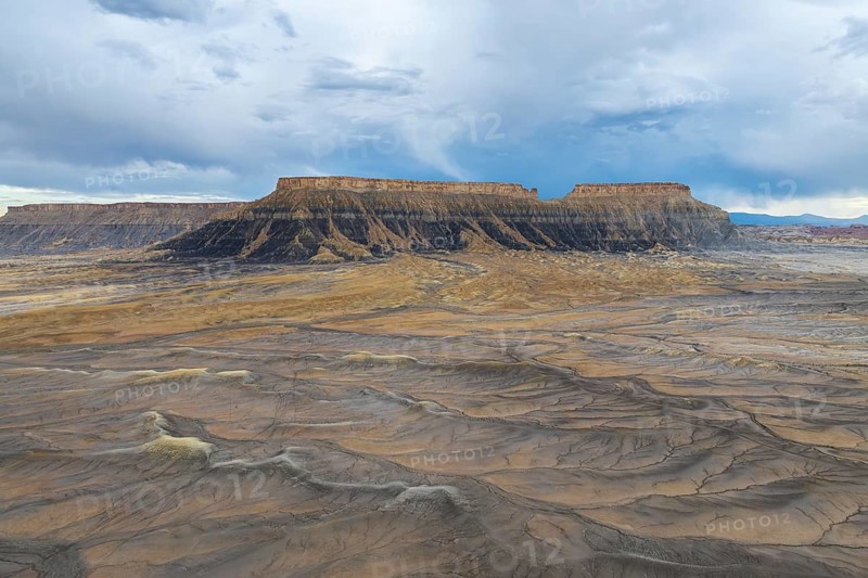 A breathtaking view of a desert plateau rising under a vast, cloudy sky, showcasing layers of sediment and earth tones, evoking a sense of timelessness and natural wonder in Hanskville, Utah