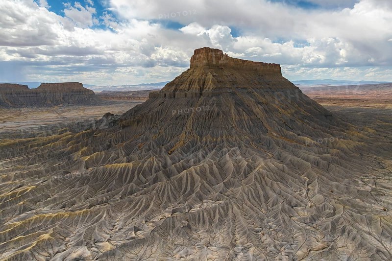 A striking aerial view of a weathered plateau with deep ridges and a barren landscape, under a dramatic sky filled with clouds, capturing the rugged beauty of nature in Hanskville, Utah