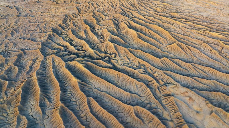 Aerial view of Caineville Mesa's rugged landscape. Eroded valleys and golden hues capture the desert's intricate textures, creating a stunning natural pattern in Utah's wilderness